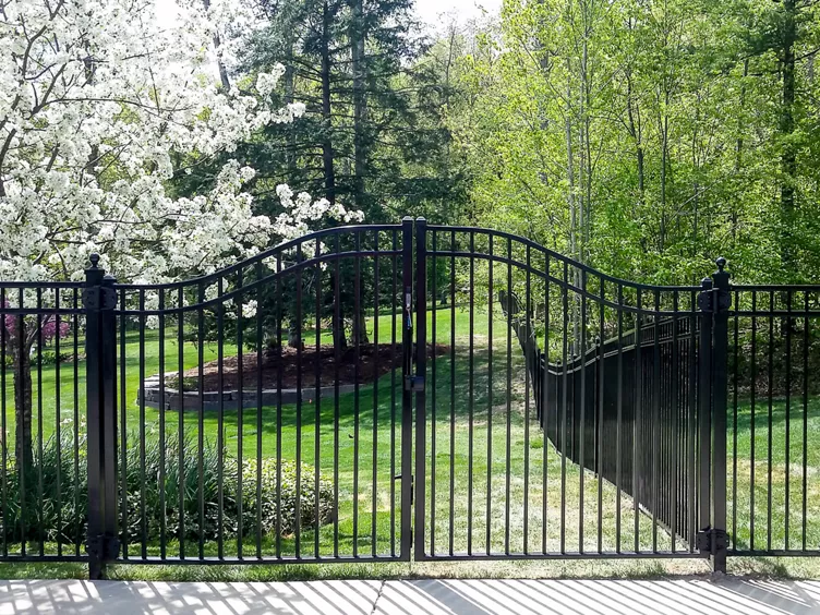 Black ornamental iron arched driveway gate with landscaping — RKC Wood Care Pros