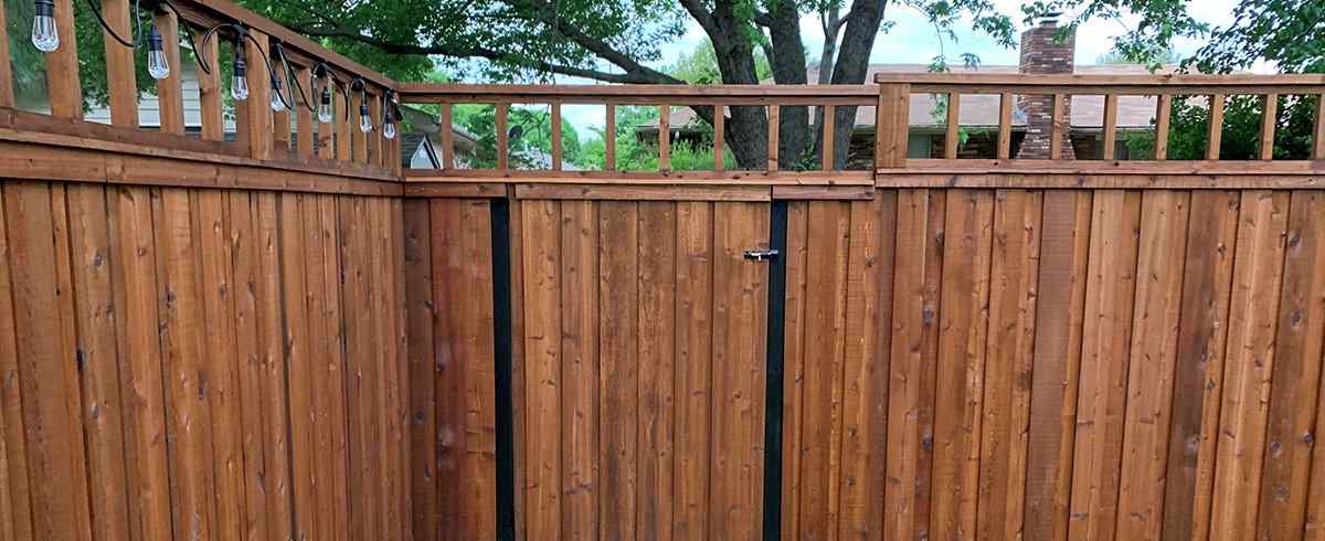 Stained cedar privacy fence with walk gate, lattice top rail, and string lights — RKC Wood Care Pros
