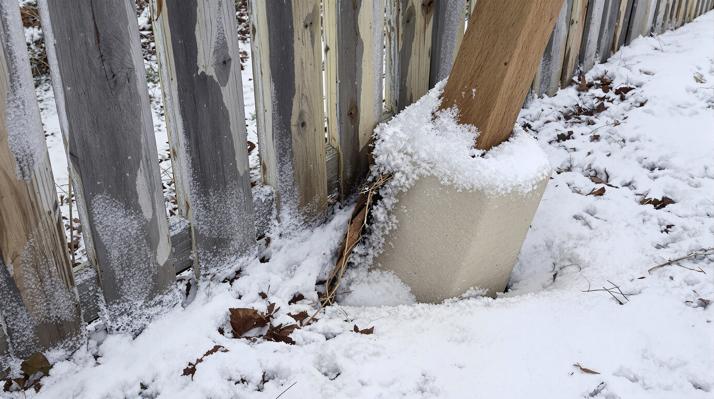 Freeze-thaw heaved fence post with exposed concrete footing in a Kansas City winter — RKC Wood Care Pros