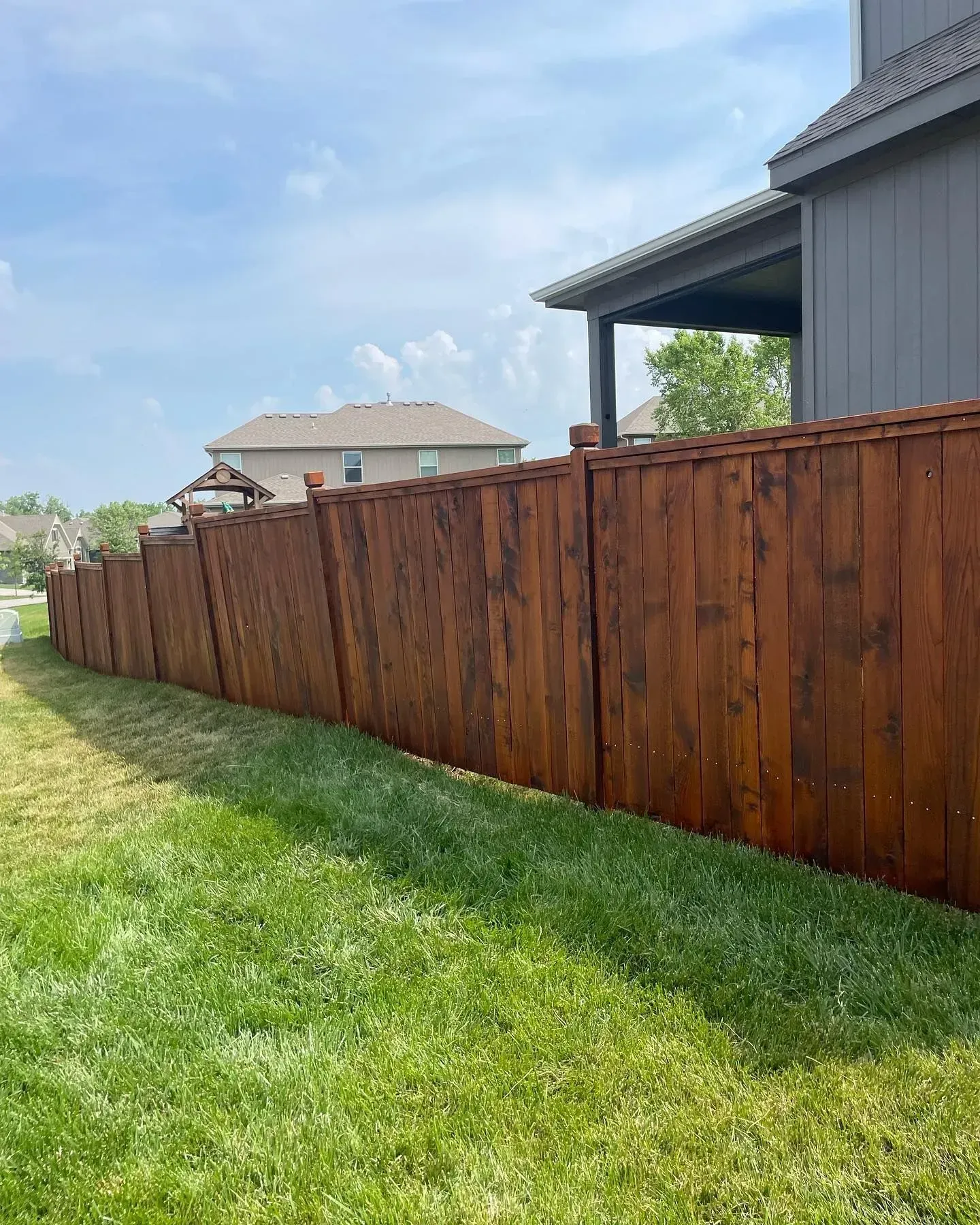 Dark-stained cedar privacy fence with fresh finish along a Kansas City suburban yard — RKC Wood Care Pros