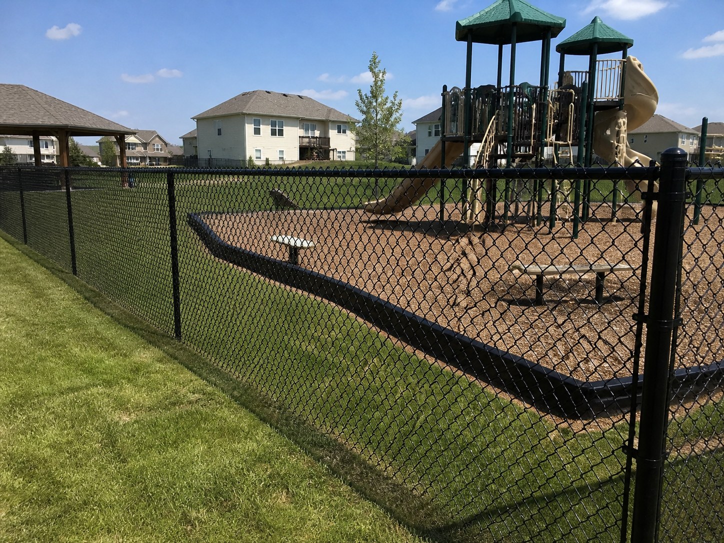 Black vinyl-coated chain link fence around a suburban playground in Kansas City — RKC Wood Care Pros
