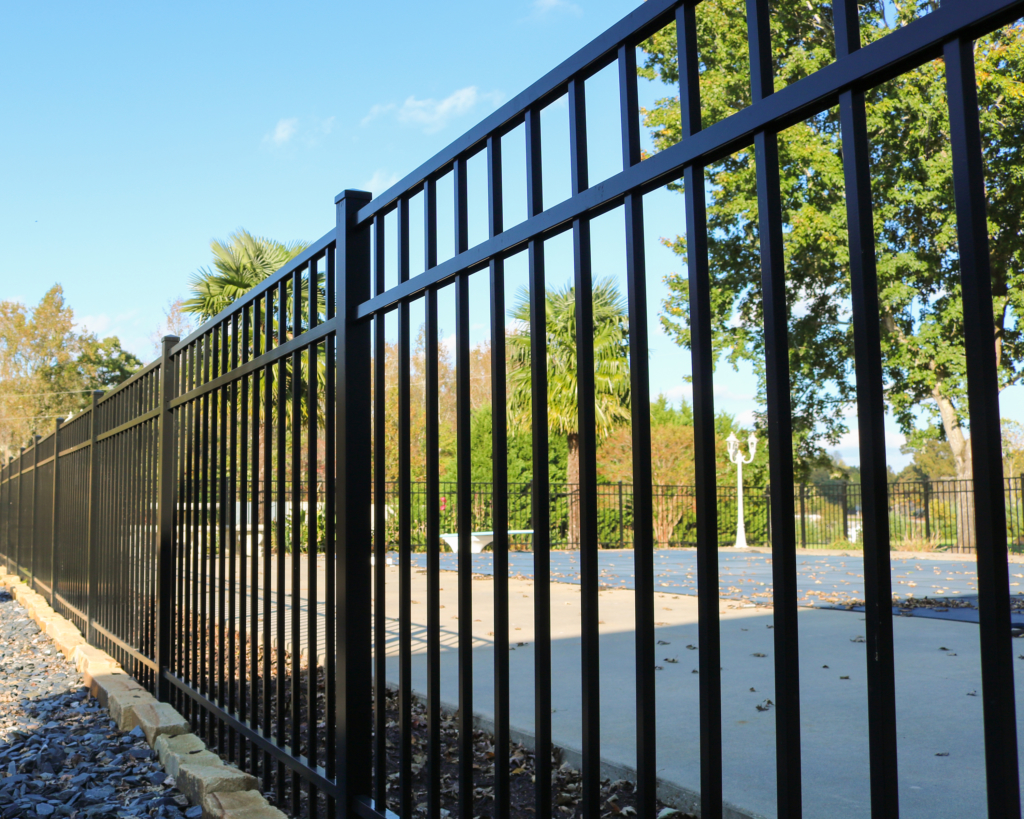 Black aluminum ornamental fence with flat-top pickets along a commercial parking lot — RKC Wood Care Pros
