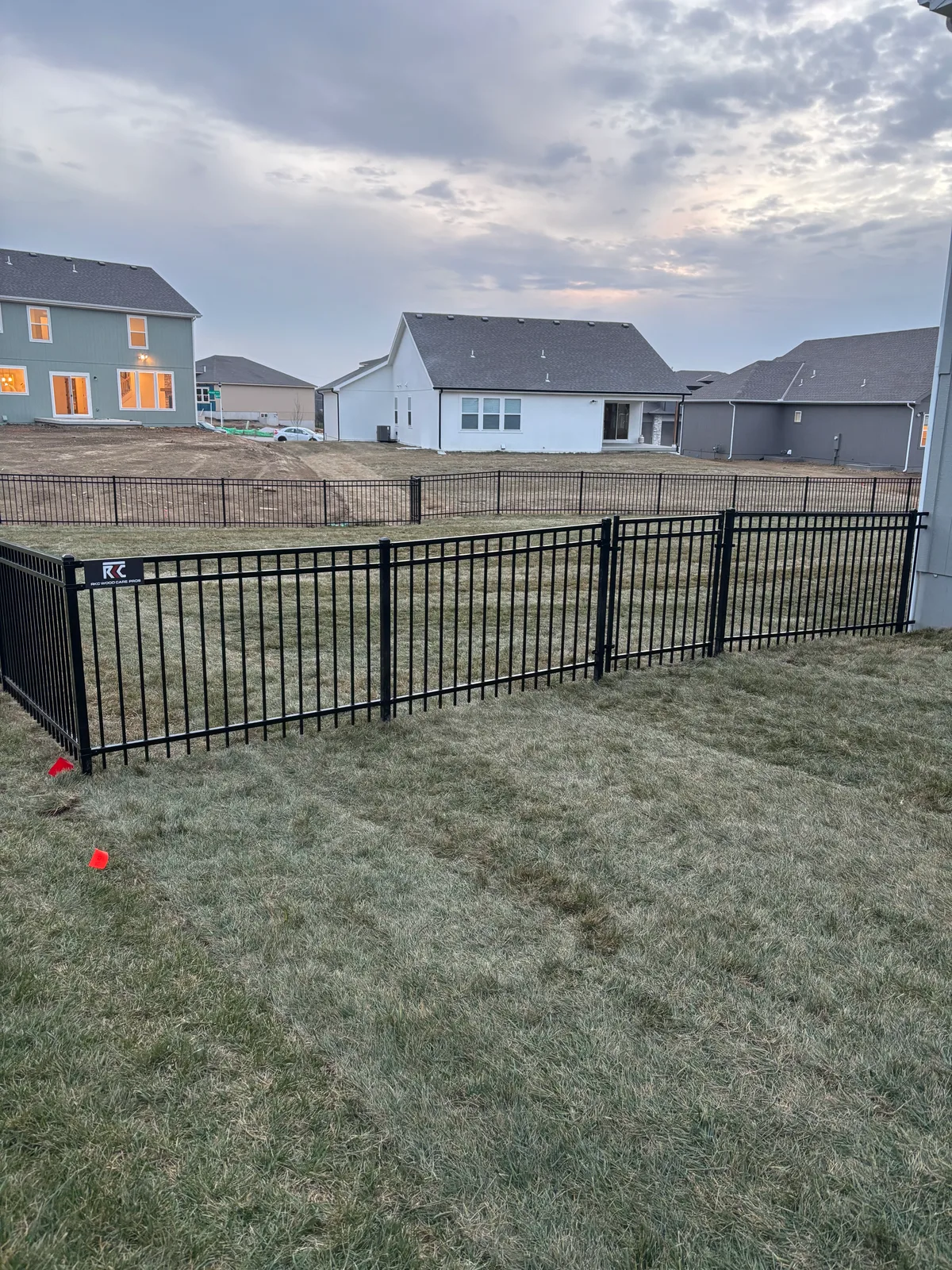Far-end view of new black iron fence line on bare dirt lot in Overland Park, KS