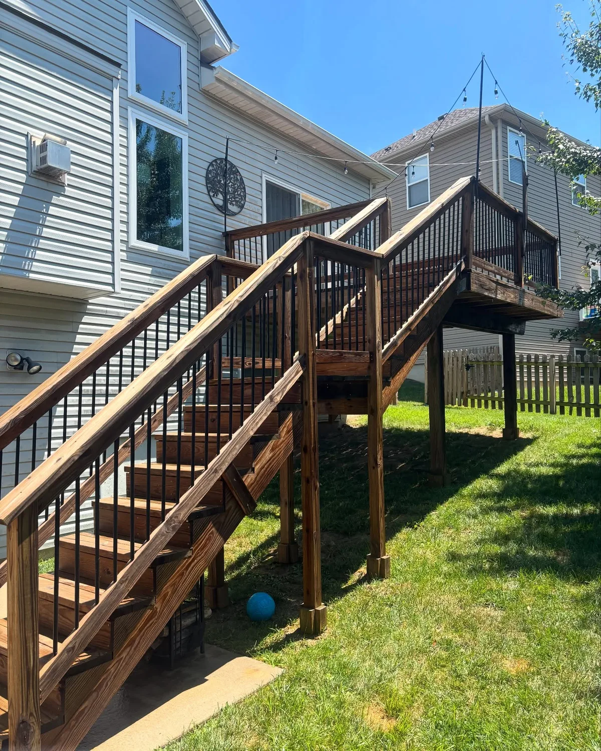 Stair and railing view of stained elevated deck in Stilwell, KS on clear blue sky day