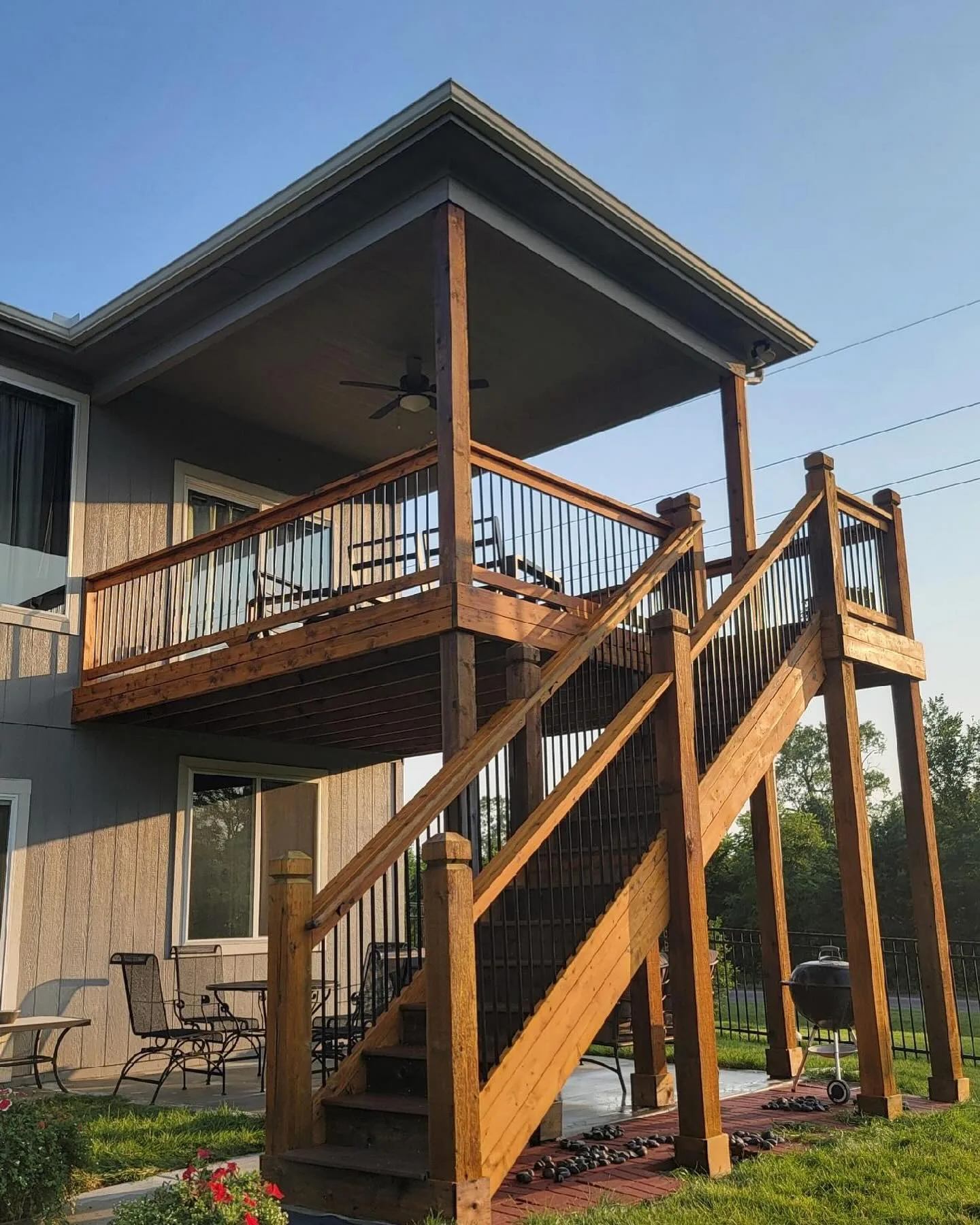 Tall two-level elevated deck with covered upper level stained in Oak Grove, MO — morning golden light